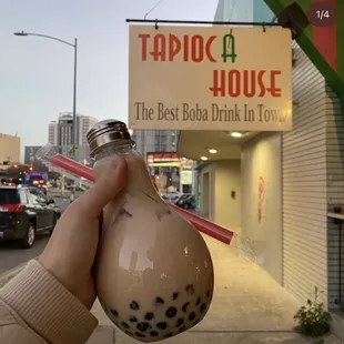 a hand holding a drink in front of a tapioca house