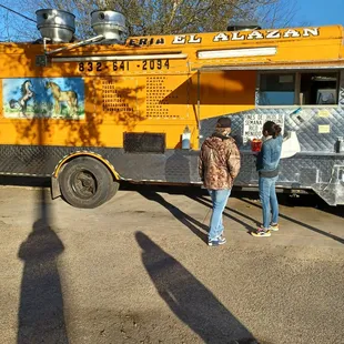 two people standing in front of a food truck