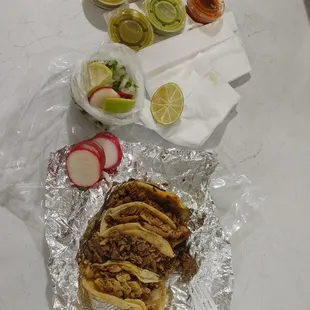 a plate of tacos, lime slices, and sliced radishes