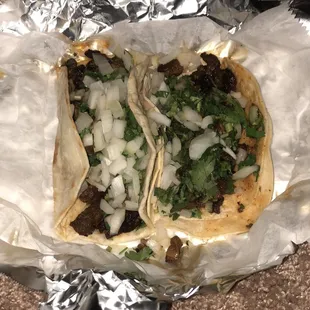 One fajita taco on flour with cilantro and onions, one fajita taco on corn with light onions and cilantro