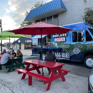 people sitting at picnic tables under umbrellas