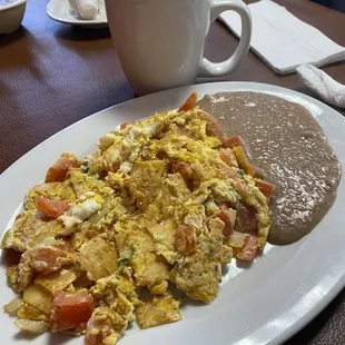 a plate of scrambled eggs with a side of beans and a cup of coffee