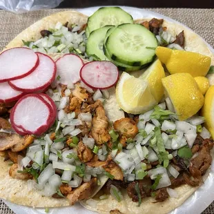 Al pastor and chicken tacos with sides of cucumber, radish, and lemons.