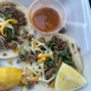 carne asada taco with cheese and cilantro. red sauce and juicy lemons