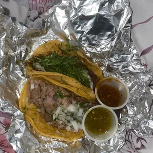 One Barbacoa and one Carnitas taco with onion and cilantro. Green and red salsa on the side.