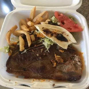 a steak and french fries in a styrofoam container
