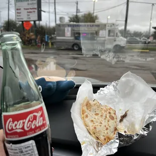 a person holding a bottle of coca cola and a flatbread