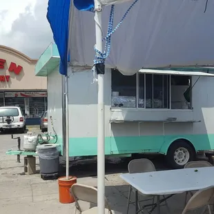 Nondescript trailer in a parking lot with seating under an awning.