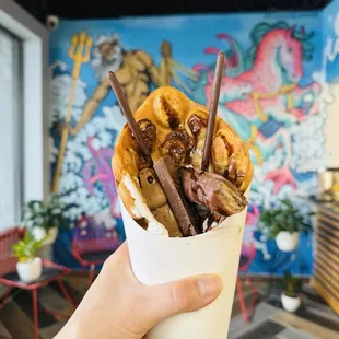 a hand holding a paper cup filled with ice cream and chocolate