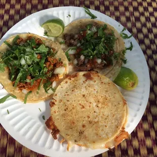 One taco al pastor, one with beef cheeks, and one quesadilla on corn tortillas with chicken.