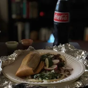 A tamale and two carnitas tacos with salsa and a Mexican coke.