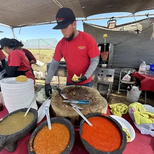 Molcajetes full of salsa and a worker about to chop of delicious carne asado in this stump cutting board
