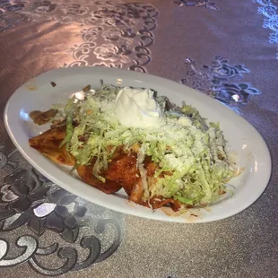 Enchiladas Made with a corn tortilla covered with red salsa, potatoes, lettuce, cheese and sour cream.