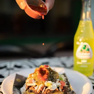 a hand sprinkling sauce over a plate of food