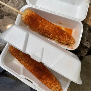 two pieces of corn on a stick in a styrofoam container