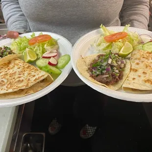 a woman holding two plates of tacos