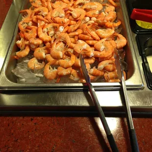 a tray of shrimp with tongs