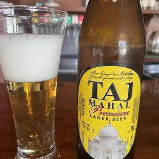 a bottle of taj mahal lager beer next to a glass of lager beer