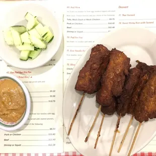 Chicken satay with peanut satay sauce and a side of cucumbers.