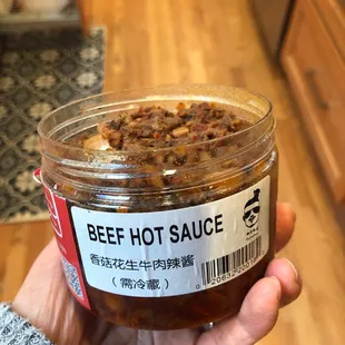 a hand holding a jar of beef hot sauce