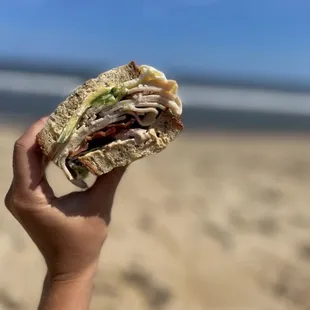 a person holding a sandwich on the beach