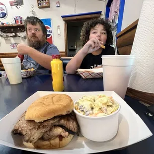 two people sitting at a table with a sandwich and coleslaw