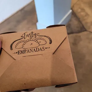 a hand holding a box of tasty empanadas