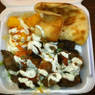 Lamb kabob on salad with potatoes and pita.