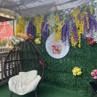 a wicker chair in front of a wall of flowers