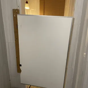 Bathroom stall door is a whiteboard held up with cabinet hinges and a 2x4.