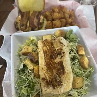 Caesar salad with mahi mahi and burger/tots in the background
