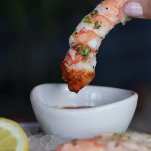 a person dipping shrimp into a bowl of sauce