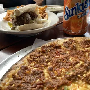 Soujouk flatbread (spicy) and falafel sandwich (in samoon) with fries and drink (background)