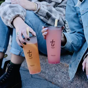 a woman sitting on a curb with two drinks