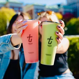 two women sitting on a bench, one holding a drink and the other holding a drink