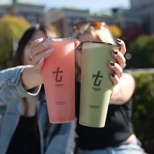 two women sitting on a bench, one holding a drink and the other holding a cup