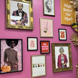 a pink wall with a variety of framed art