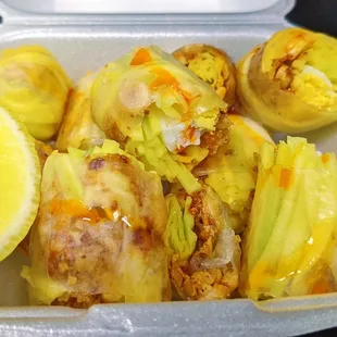  a tray of stuffed cabbage rolls with lemon wedges