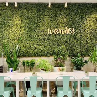 a table and chairs in front of a wall of plants