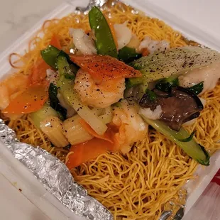 a take out container of noodles with shrimp and vegetables