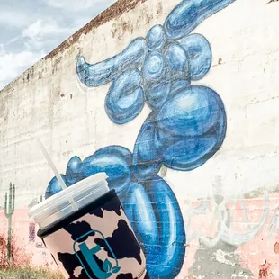 a hand holding a coffee cup in front of a graffiti wall