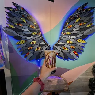 a hand holding a coffee cup with wings painted on it