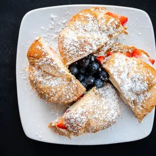a plate of pastries with powdered sugar and blueberries