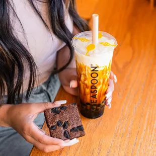 a woman holding a brownie and a drink