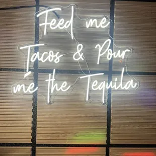 a neon sign that reads feed me tacos and pour me the tequila