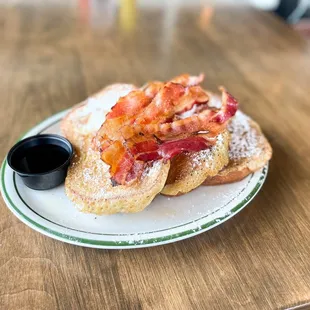 a plate of french toast with bacon and powdered sugar