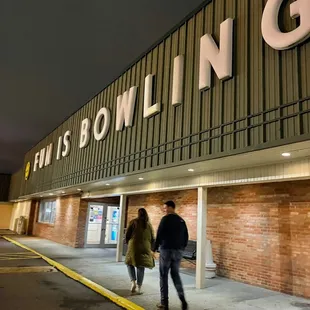 two people walking in front of a bowling alley