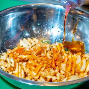 a person pouring sauce over a bowl of pasta