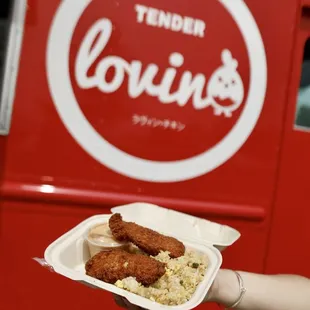 a hand holding a tray of fried chicken