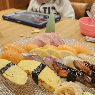 Plate of sushi with iPad kid in the back so I can eat sushi in peace [otoro sake aji engawa tamago unagi] alla amazing